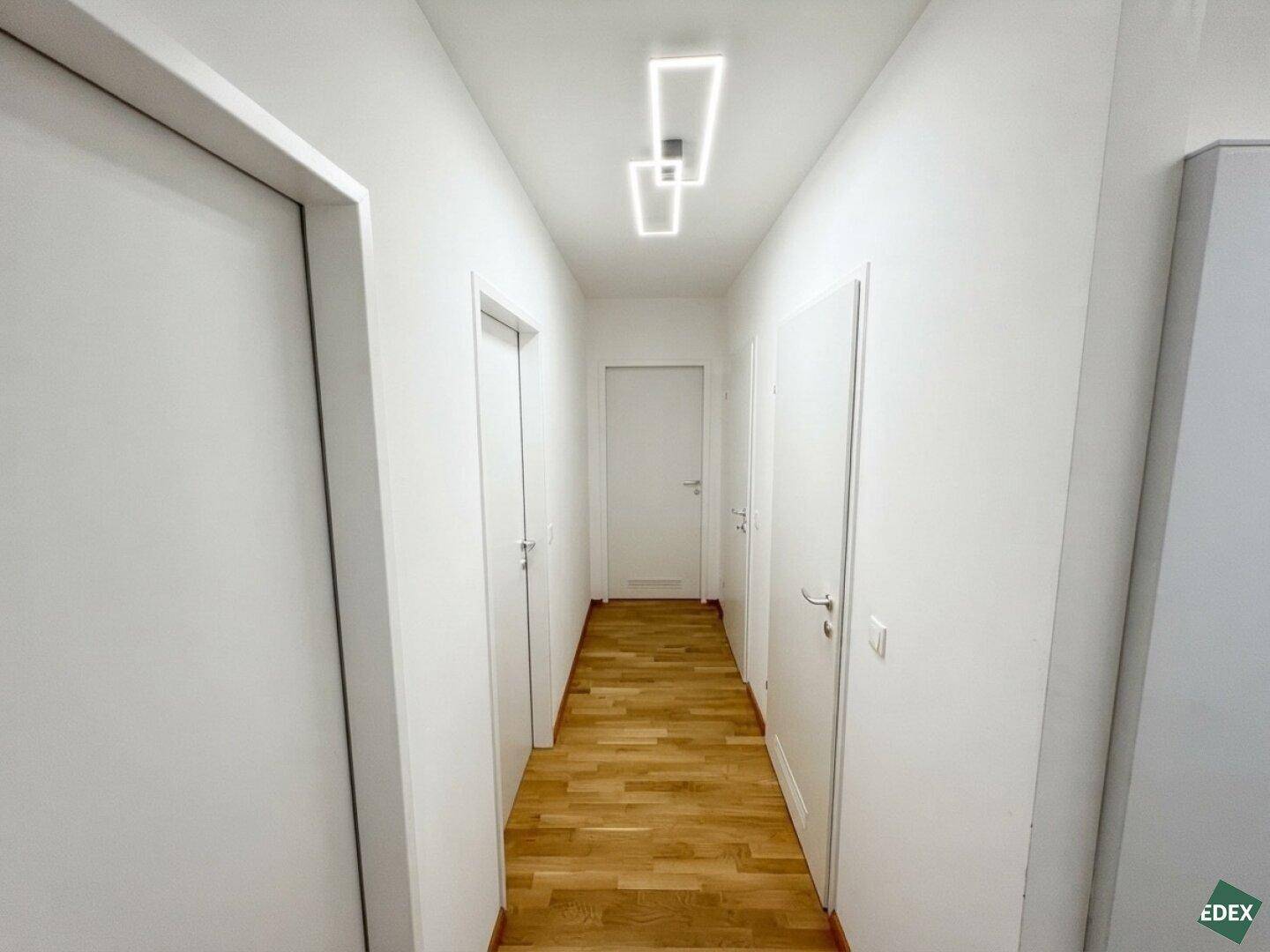 Langer Flur mit Holzboden und weißen Türen, der zu den verschiedenen Räumen der Wohnung führt.