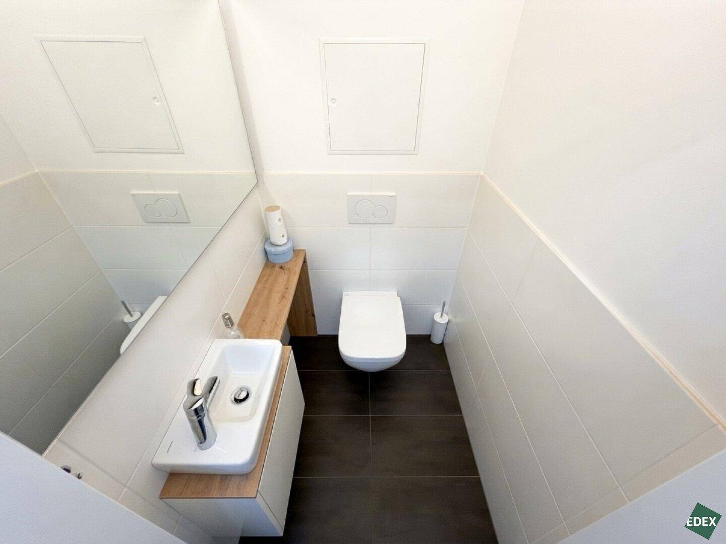 Modernes Gäste-WC mit dunklen Fliesen, wandhängendem WC und kleinem Waschbecken.