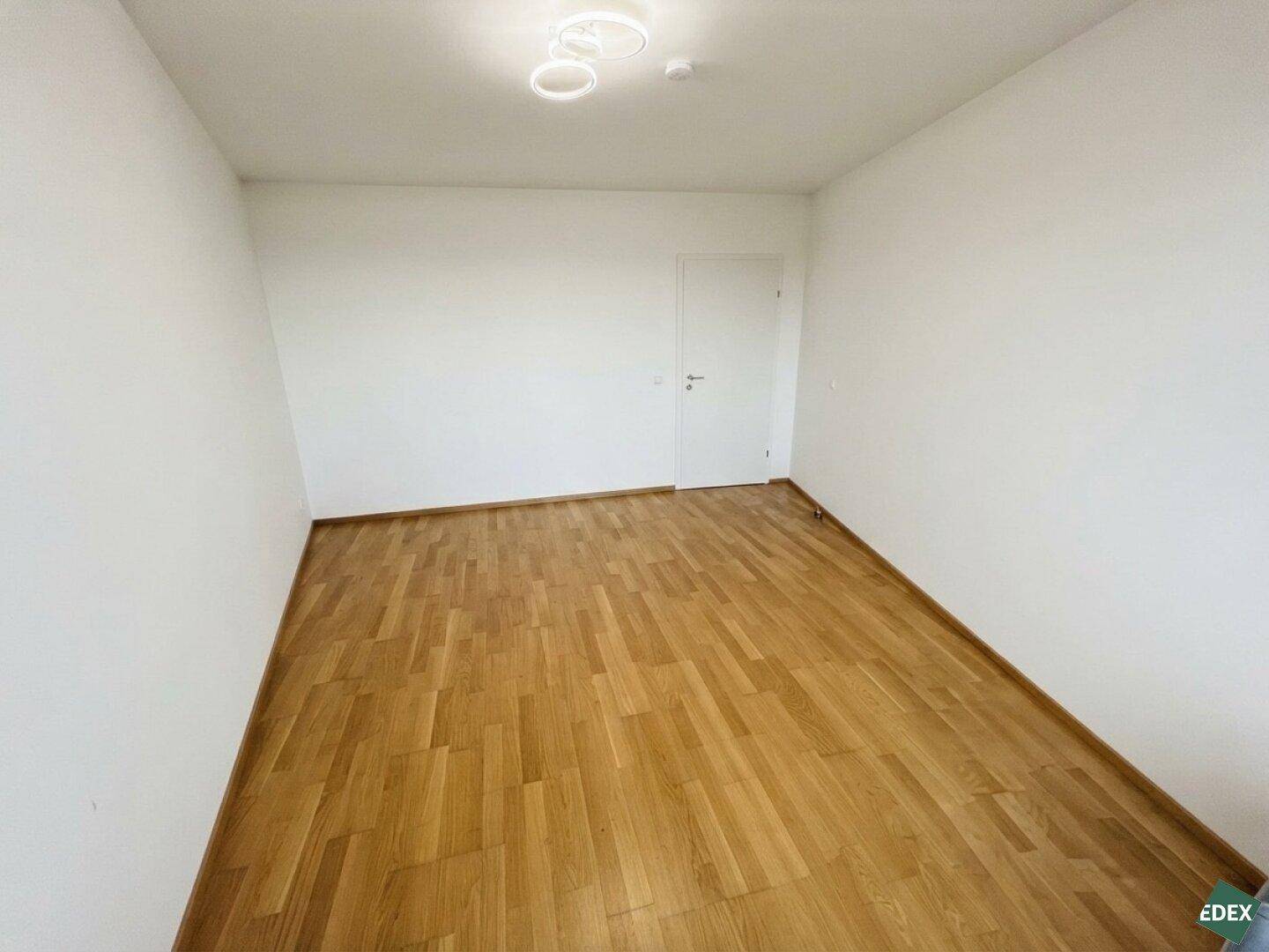 Geräumiges Zimmer mit Holzboden und weiß gestrichenen Wänden, bereit zur individuellen Gestaltung.