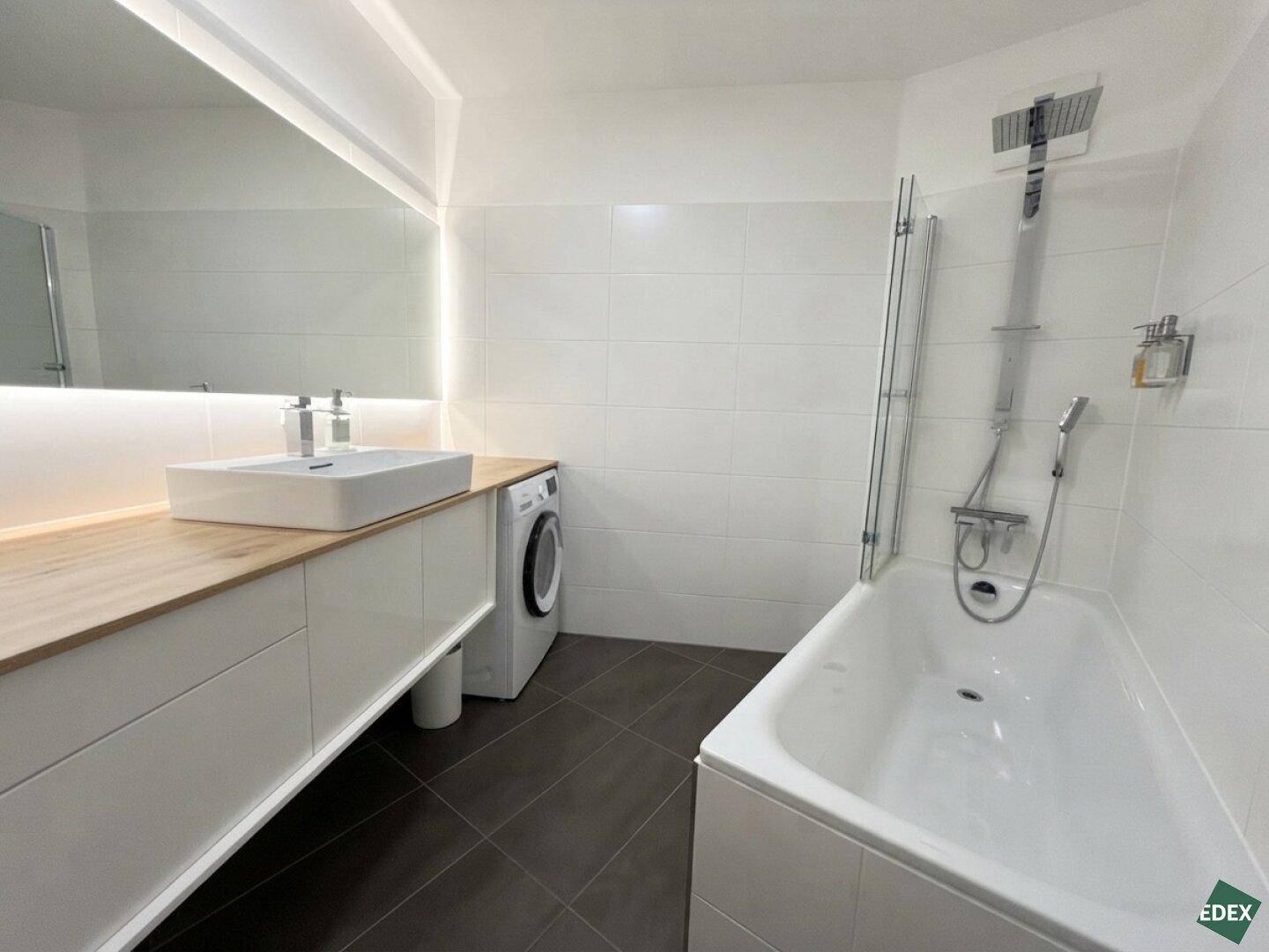 Modernes Badezimmer mit Badewanne, Dusche, Waschbecken und integrierter Waschmaschine.
