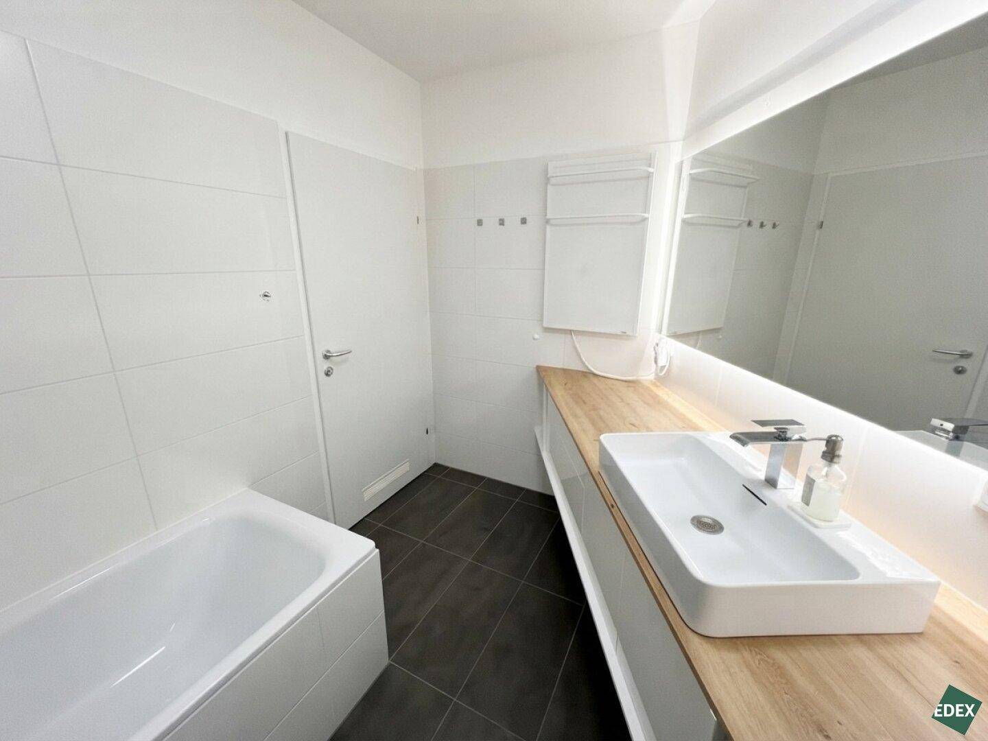 Helles Badezimmer mit großem Spiegel, modernem Waschbecken und beheiztem Handtuchhalter.