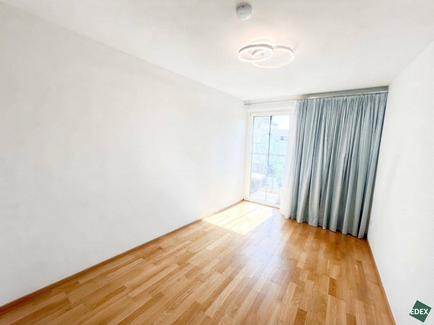 Helles Zimmer mit Holzboden und großem Fenster, das den Raum mit natürlichem Licht füllt.