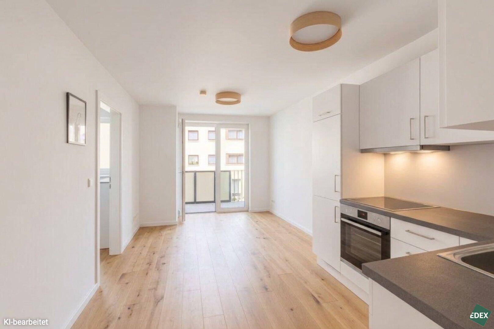 Heller offener Wohn- und Essbereich mit integrierter weißer Küche, Holzboden und Zugang zum Balkon.