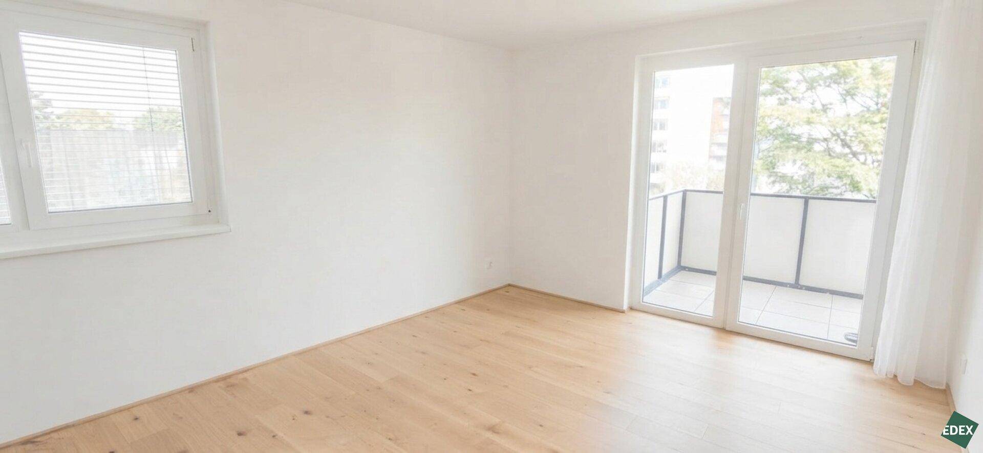 Unmöbliertes Wohnzimmer mit Parkettboden und Zugang zu einem kleinen Balkon.