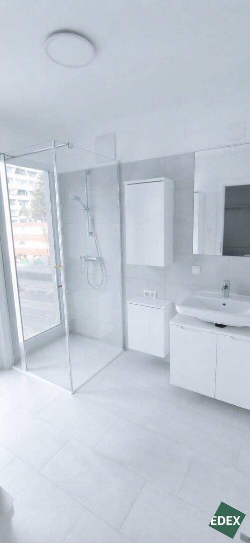 Modernes Badezimmer mit großer Glasdusche, weißen Fliesen und Waschtisch.