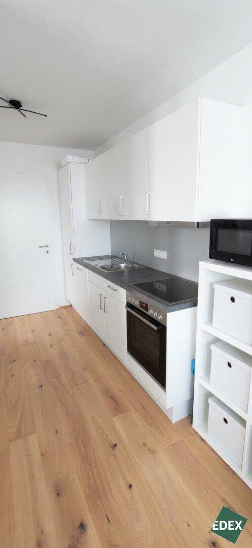 Moderne Küchenzeile mit weißen Schränken, Induktionskochfeld und Holzboden.
