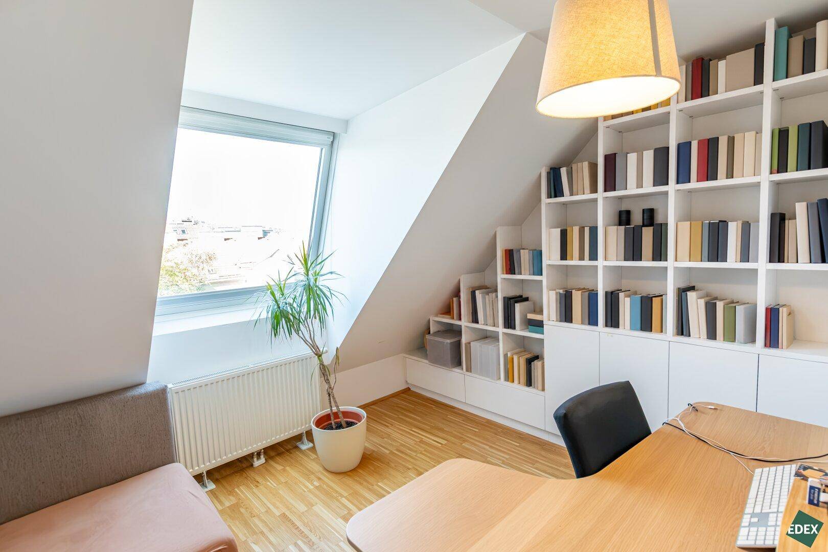 Helles Arbeitszimmer mit großem Bücherregal, Schreibtisch und Dachfenster.