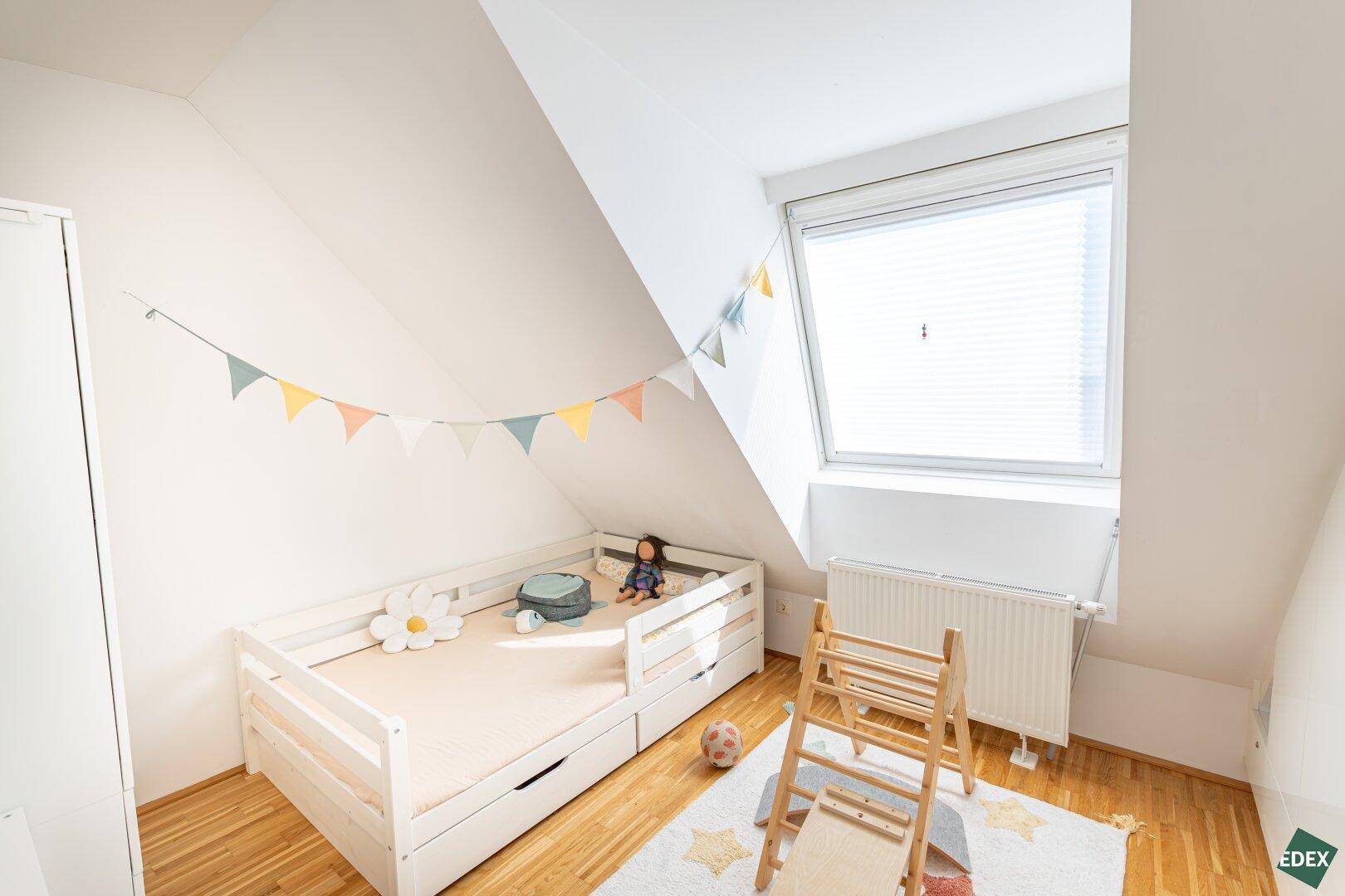 Kinderzimmer mit Holzbett, Spielgeräten und Dachschräge.