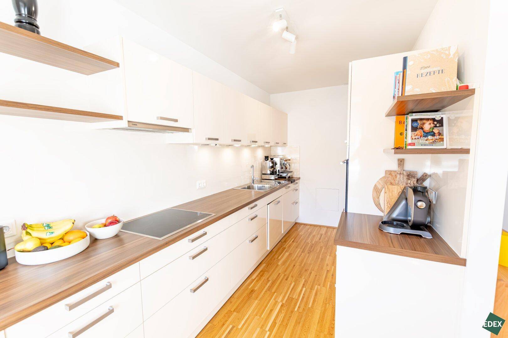 Moderne Einbauküche mit hellen Schränken, Holz-Arbeitsplatten und integrierten Geräten.