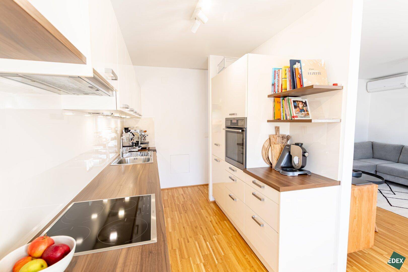 Moderne Küche mit Backofen, Kochfeld und Regalen für Kochbücher.