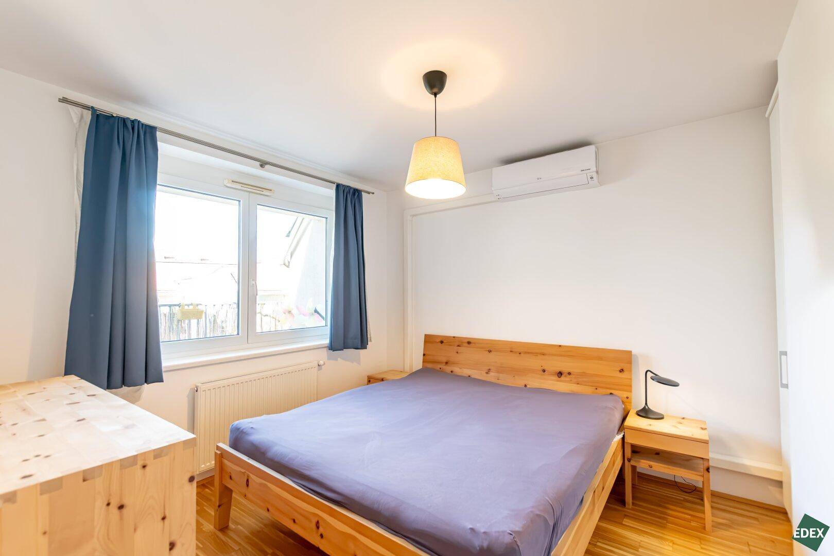 Gemütliches Schlafzimmer mit Holzbett, Holzboden und Klimaanlage.