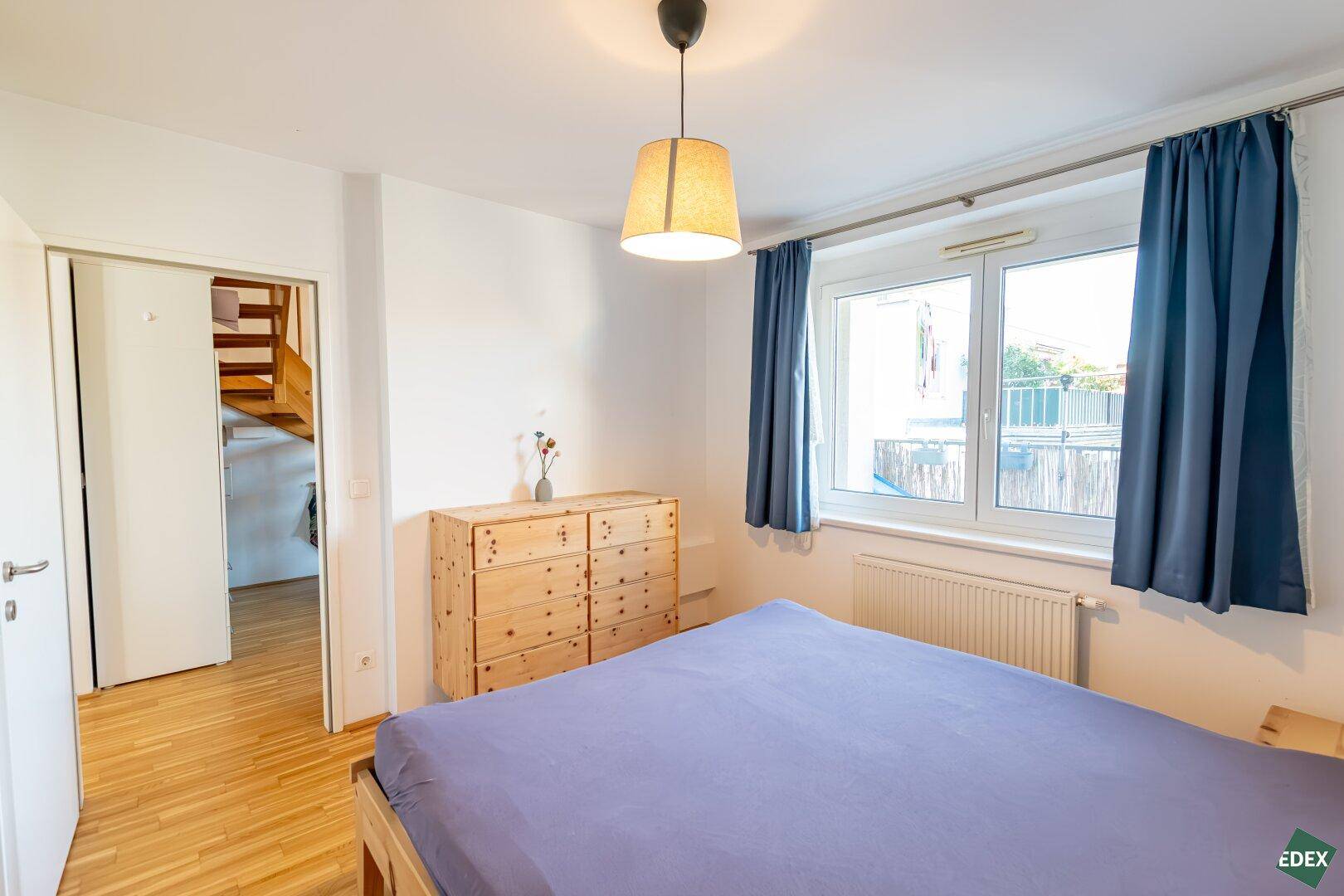 Schlafzimmer mit Holzbett, Kommode und Zugang zu einem weiteren Raum.