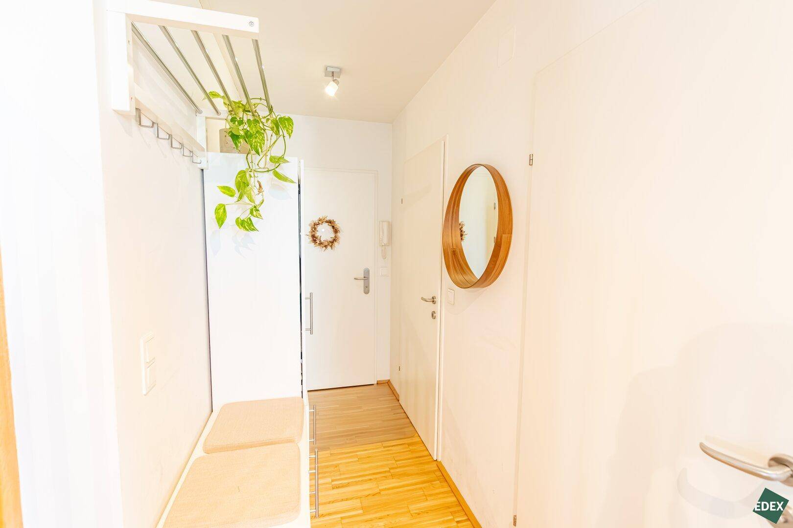 Heller Eingangsbereich mit Holzboden, Garderobe und einem runden Spiegel.