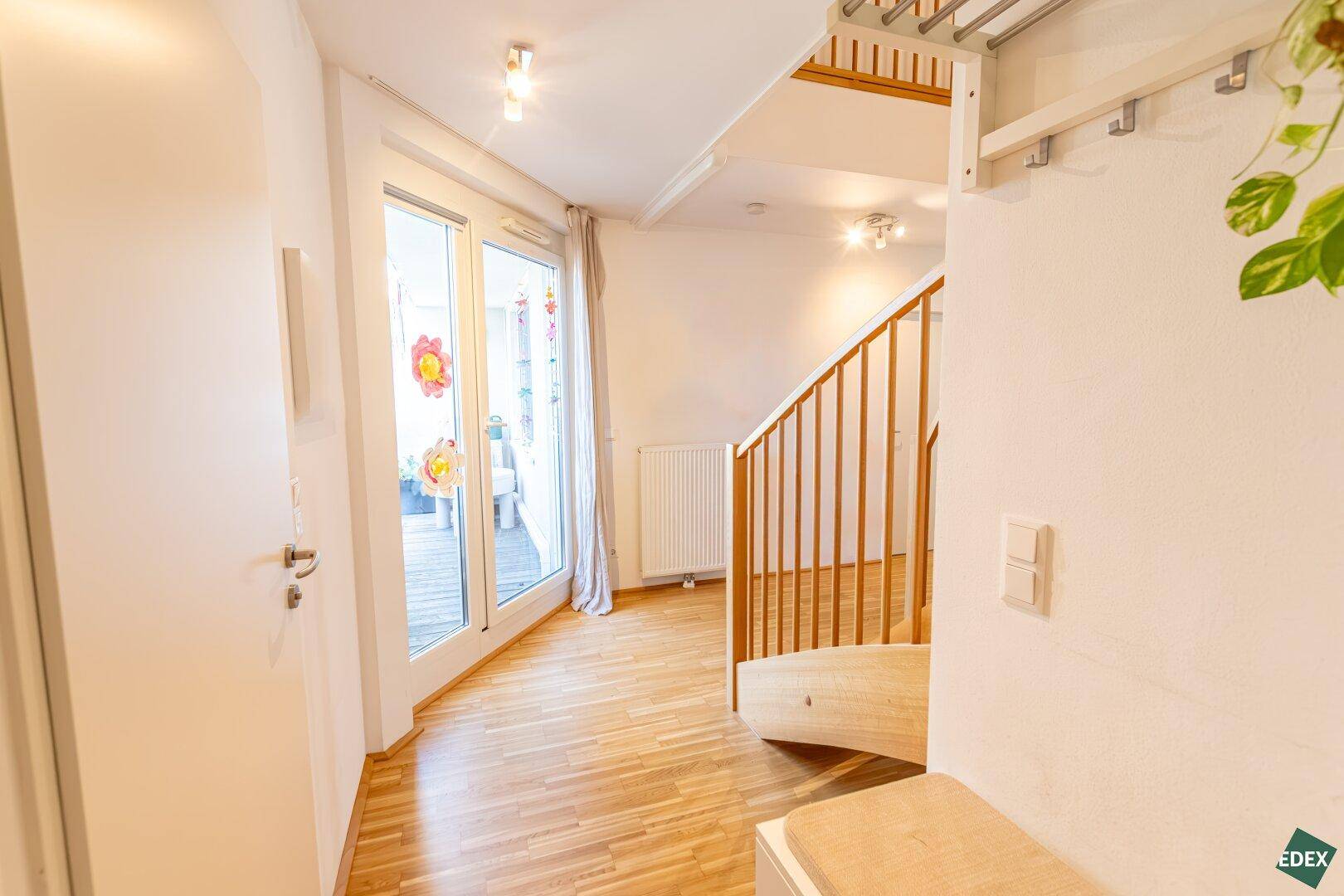 Geräumiger Flur mit Holztreppe und Zugang zu einem Außenbereich durch eine Glastür.