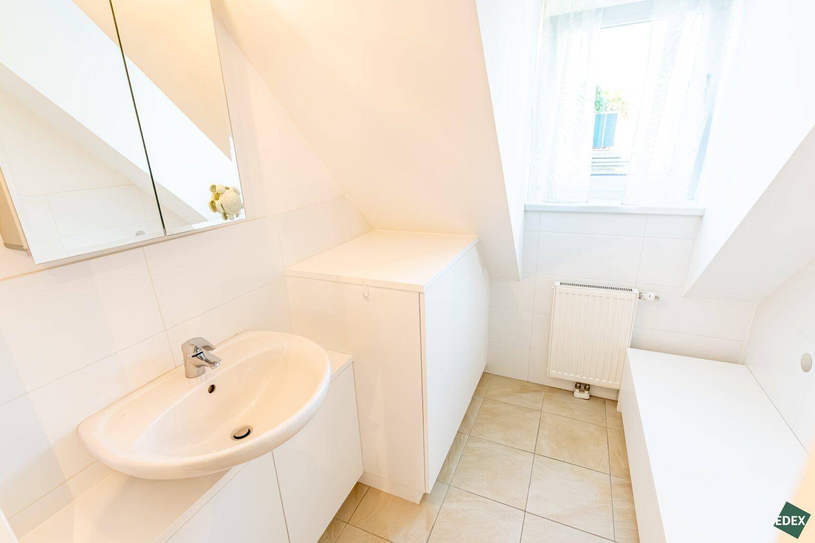 Helles Badezimmer mit Dachschräge, Waschbecken und Fenster für Tageslicht.