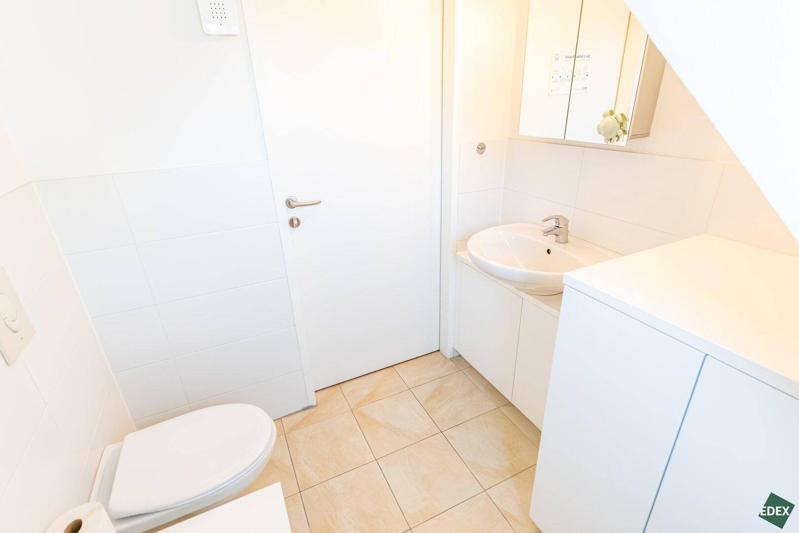 Modernes WC mit Waschbecken, Wand-WC und hellen Fliesen.