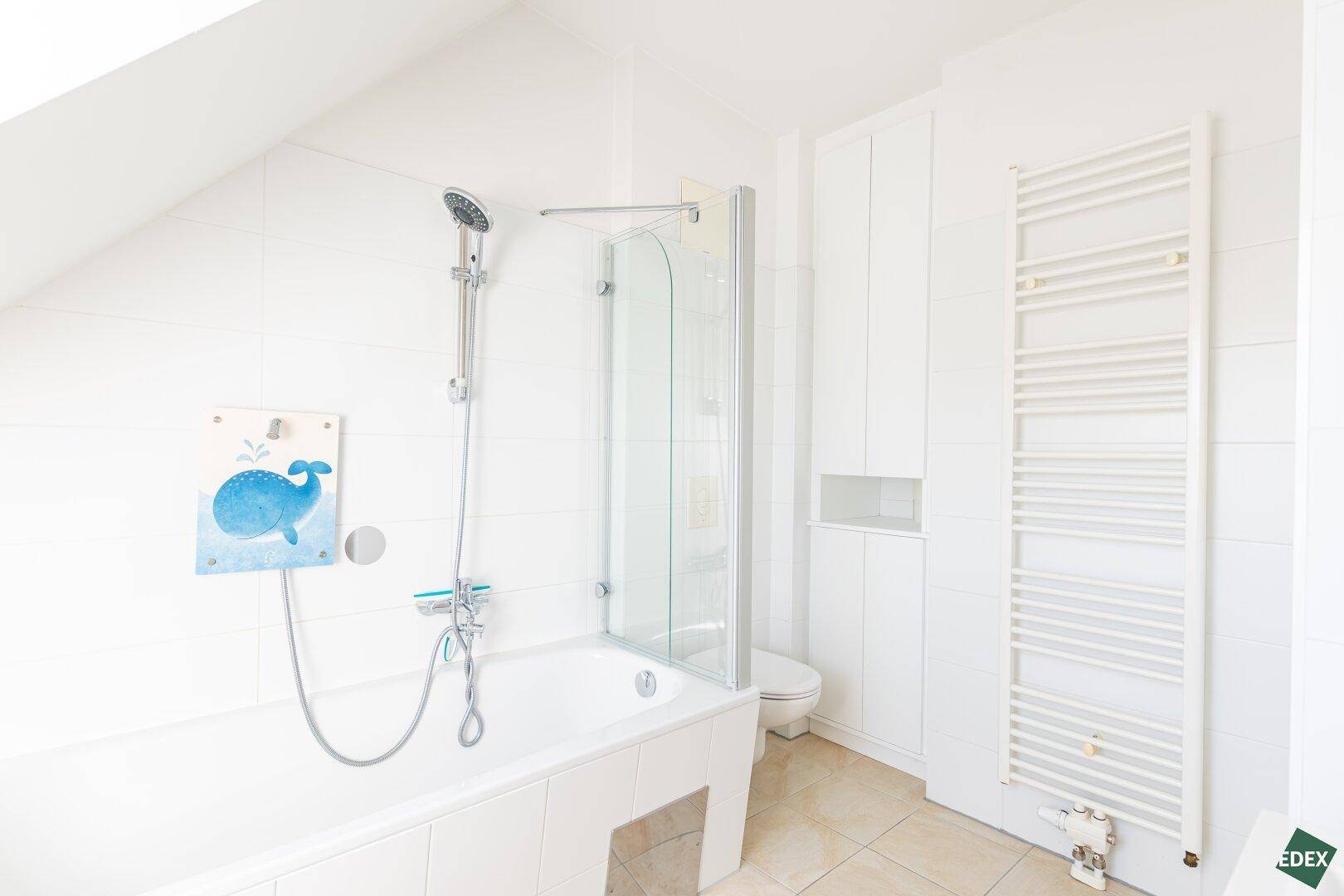 Modernes Badezimmer mit Badewanne, Duschfunktion und beheiztem Handtuchhalter.