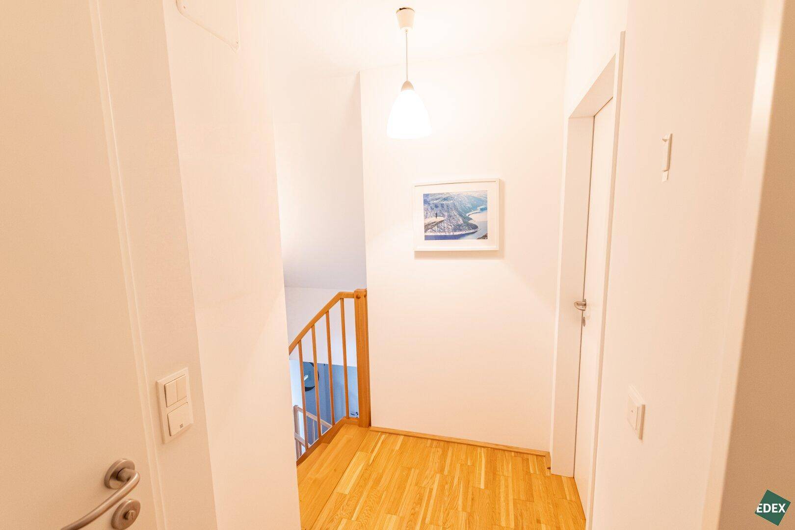 Heller Flur mit Holzboden und Treppenaufgang zu einer weiteren Etage.