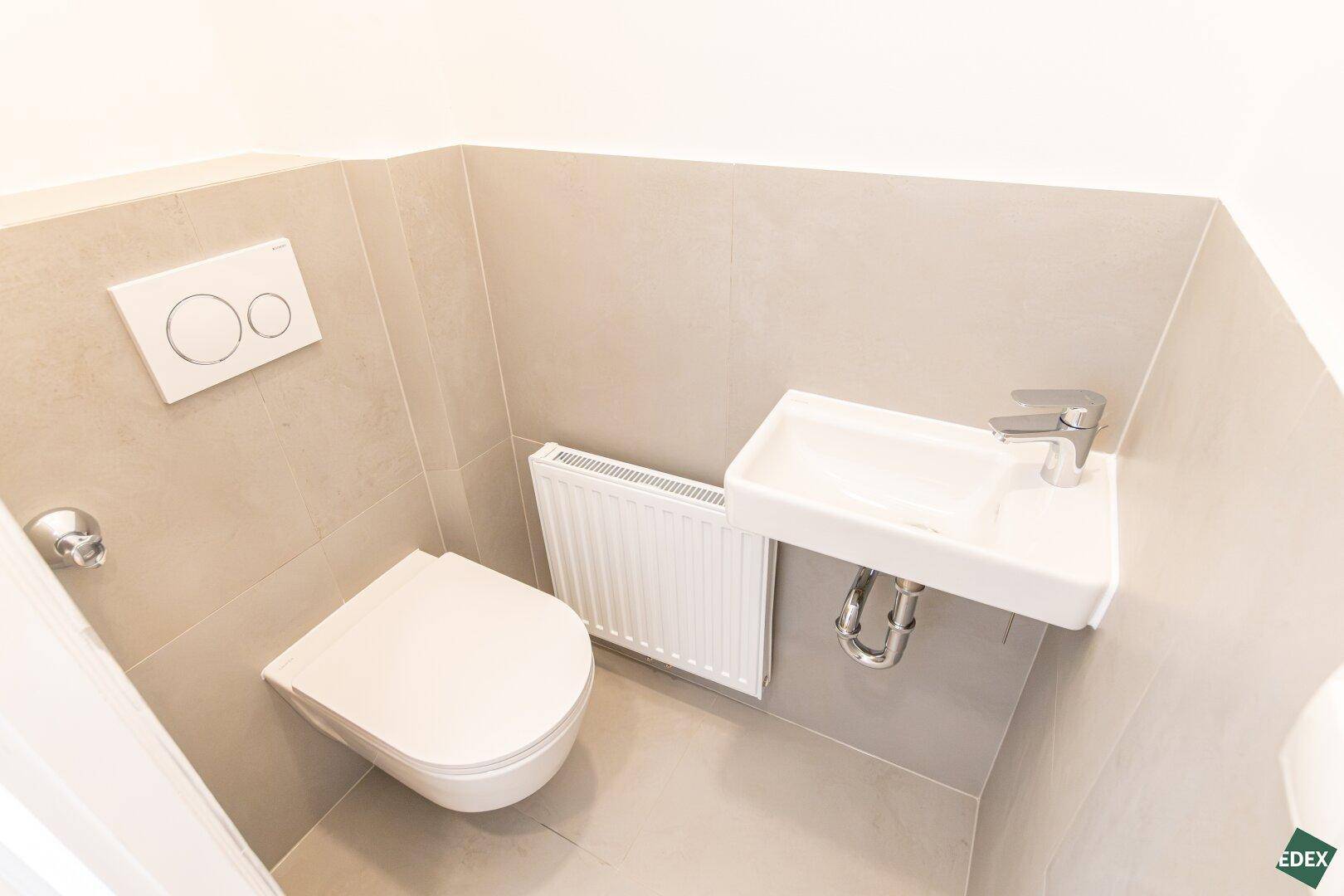 Separates WC mit wandhängender Toilette und kleinem Handwaschbecken.