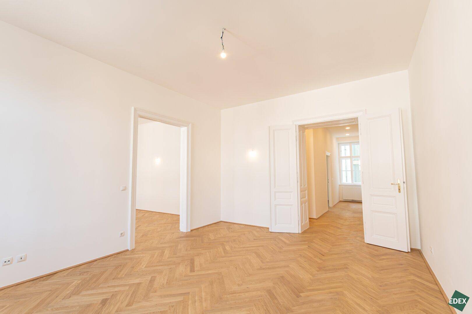 Geräumiges Zimmer mit Fischgrätparkett und mehreren Türen, bietet vielseitige Nutzungsmöglichkeiten.