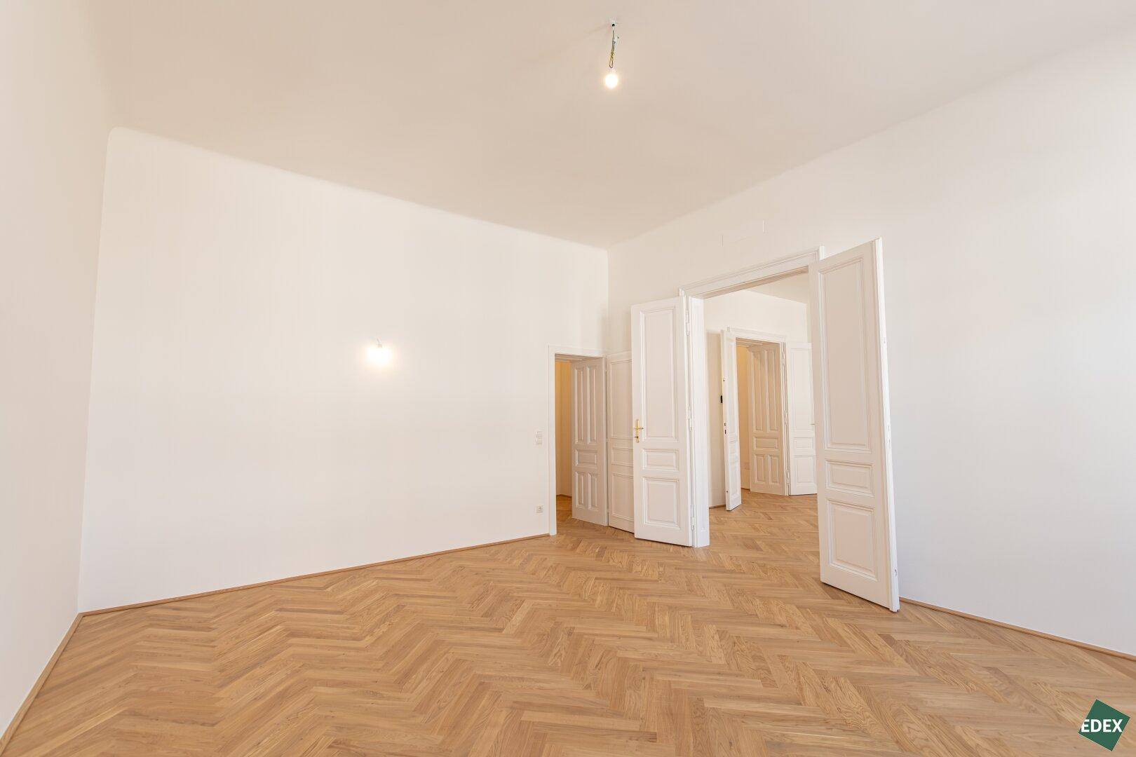 Geräumiges Zimmer mit Fischgrätparkett und hohen Türen, ideal für offenes Wohnen.