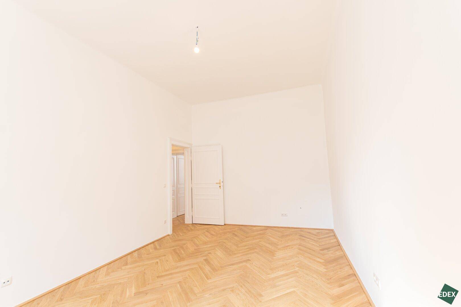 Leeres Zimmer mit Fischgrätparkett und weiß gestrichenen Wänden, bereit für neue Einrichtung.