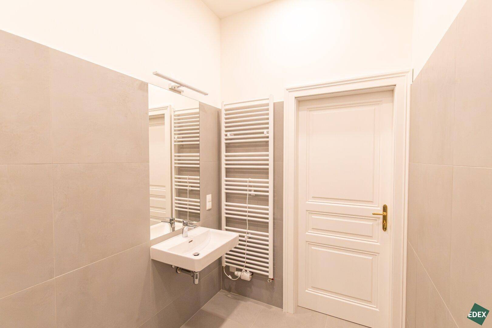 Modernes Badezimmer mit Waschbecken, Spiegel und beheiztem Handtuchhalter.