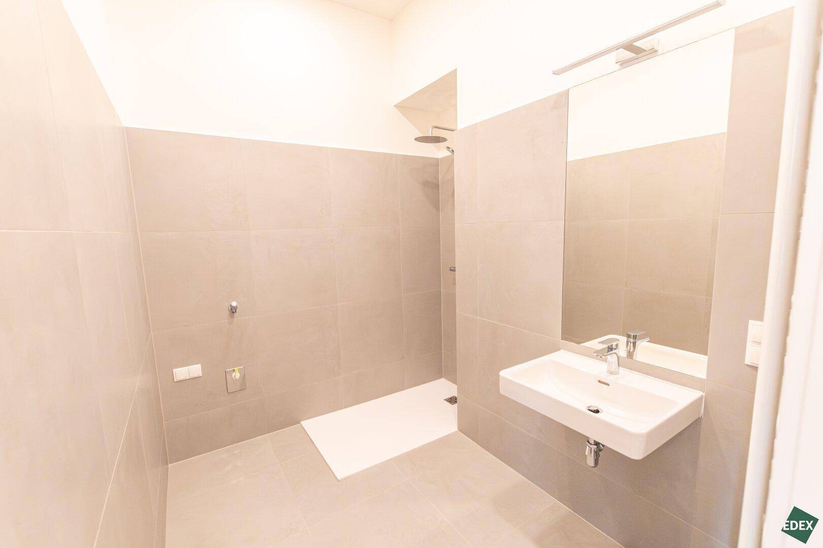 Modernes Badezimmer mit großer begehbarer Dusche und minimalistischem Waschbecken.