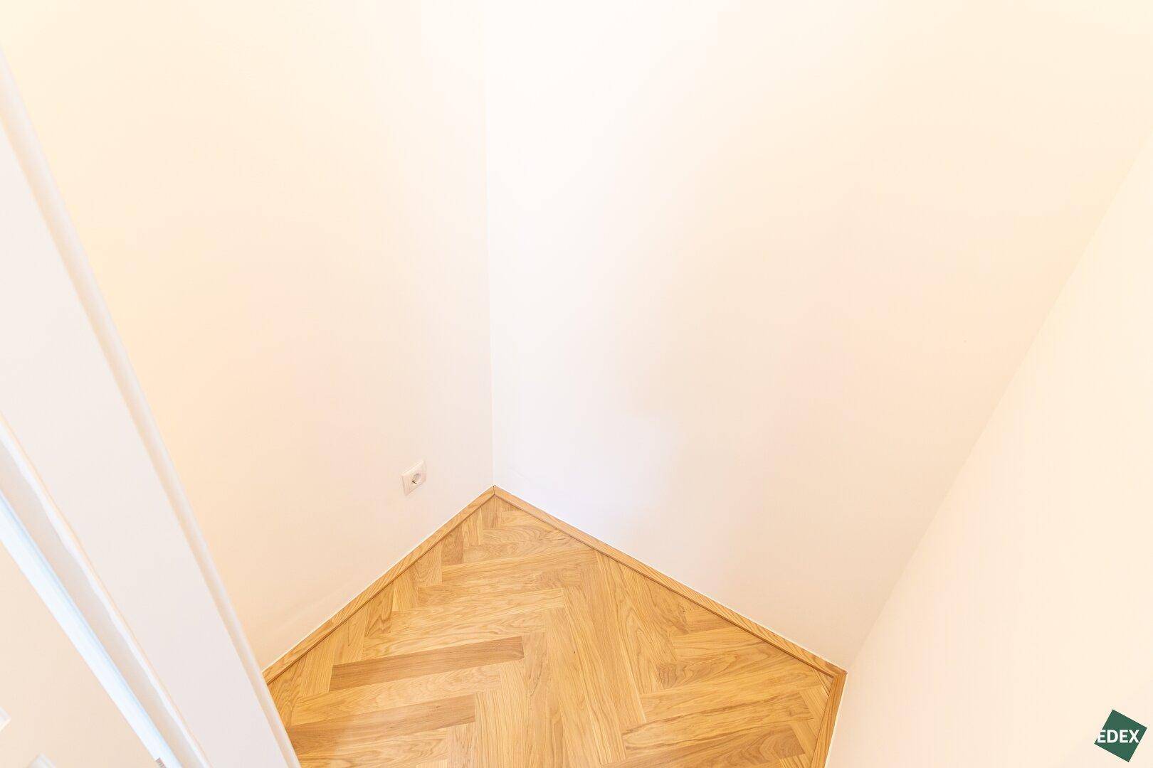 Detailaufnahme eines Raumecks mit Fischgrätparkett und hohen Wänden.