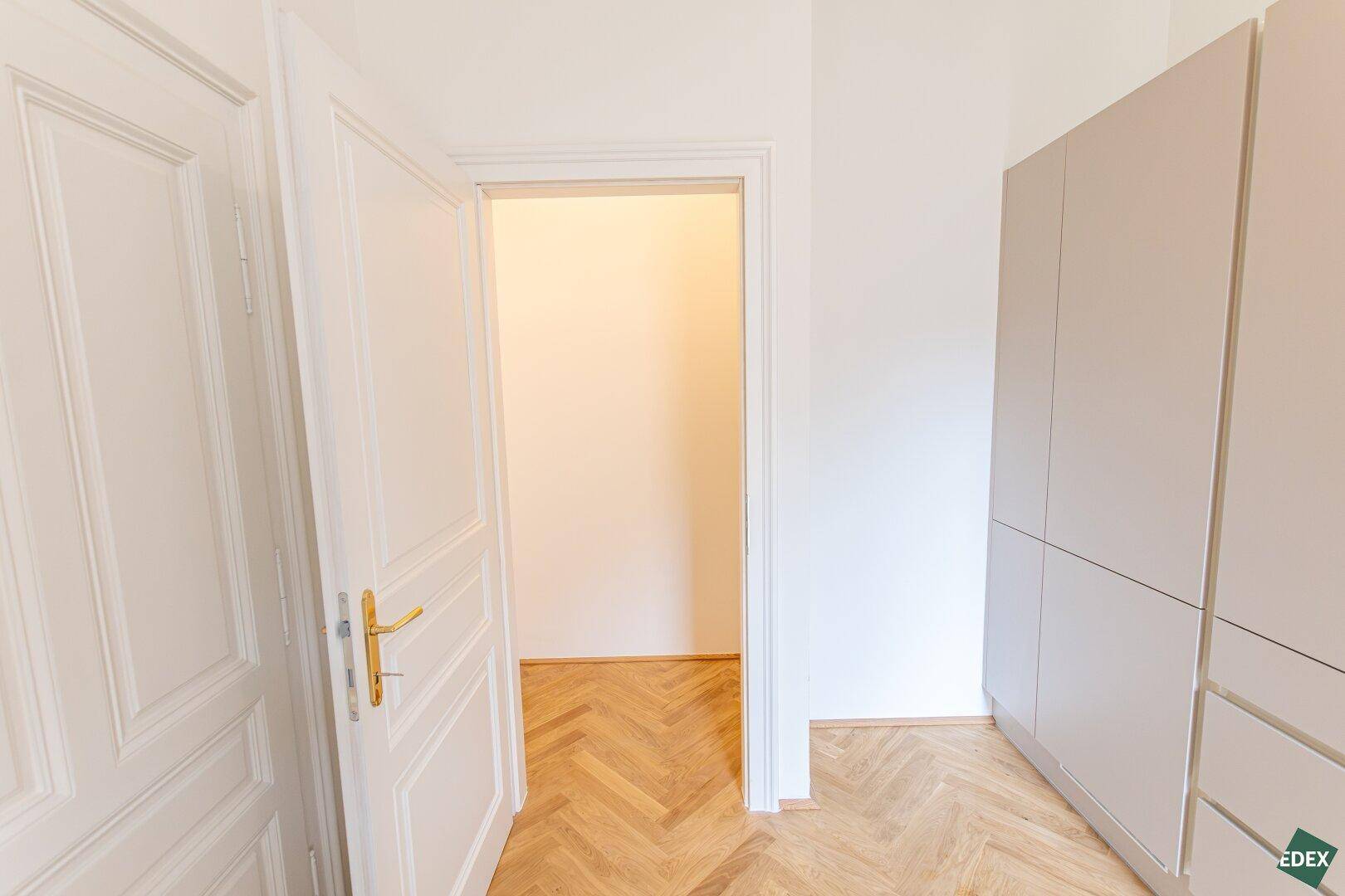 Offene Tür zu einem weiteren Raum mit Fischgrätparkett und Einbauschrank.