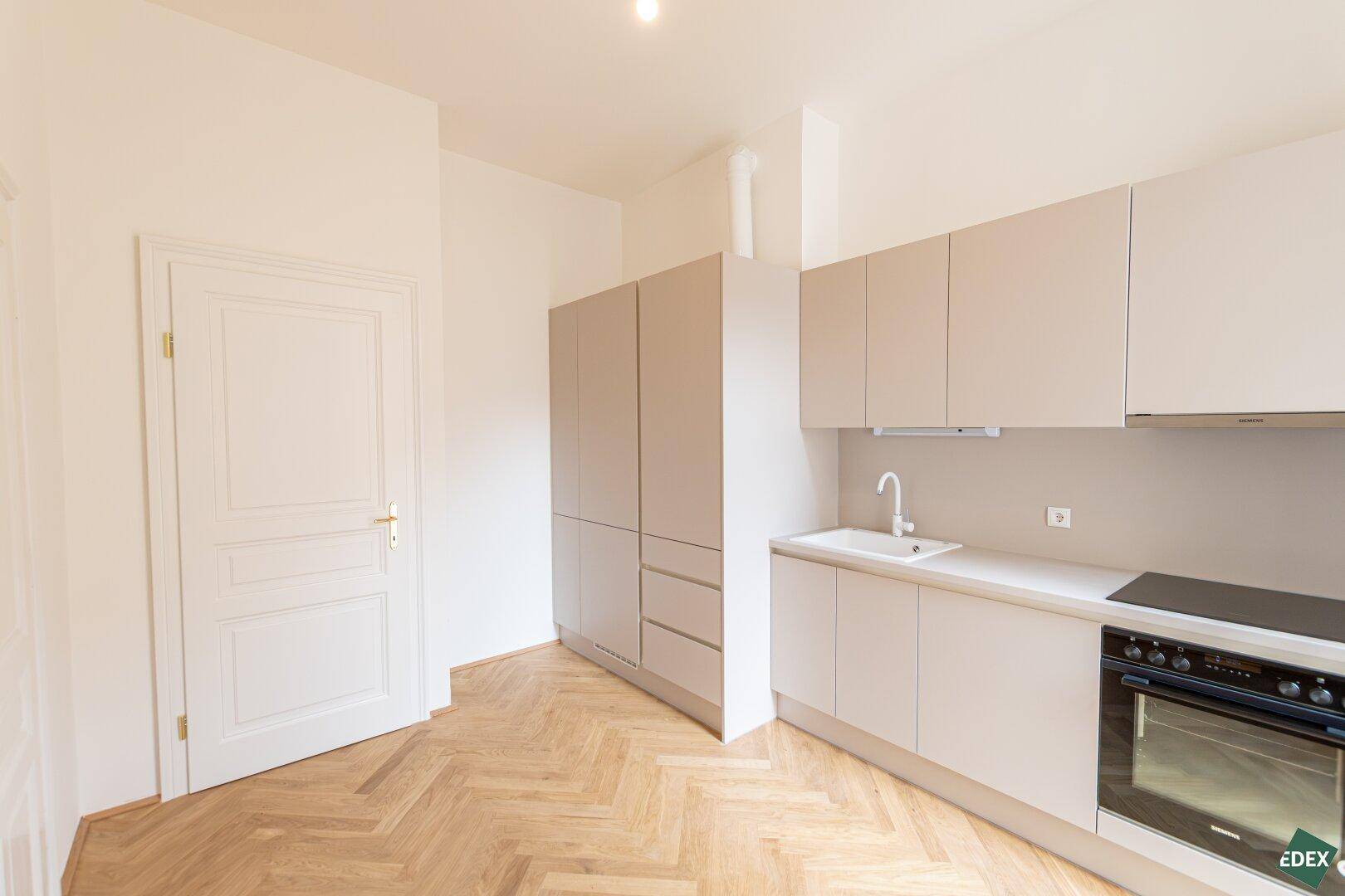 Moderne Einbauküche in Beige mit Kochfeld und Ofen, bietet effizienten Stauraum.