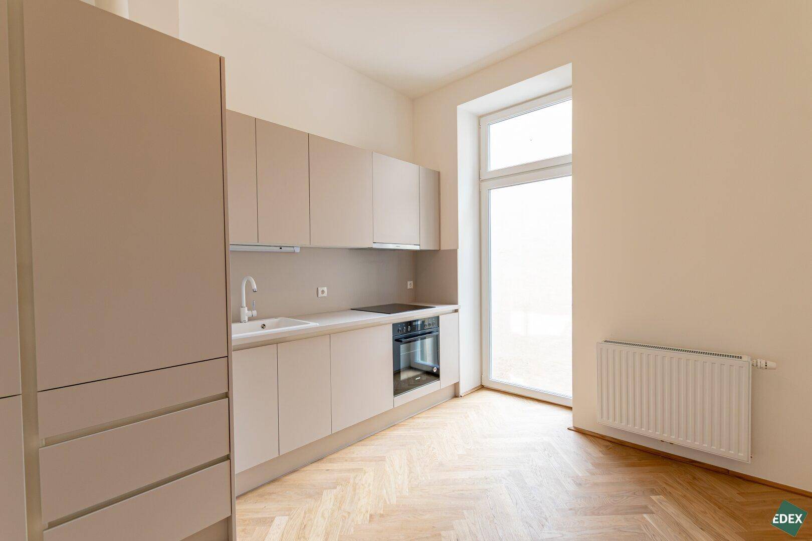 Moderne Einbauküche in Beige mit Kochfeld und Ofen, ideal für kompaktes Wohnen.