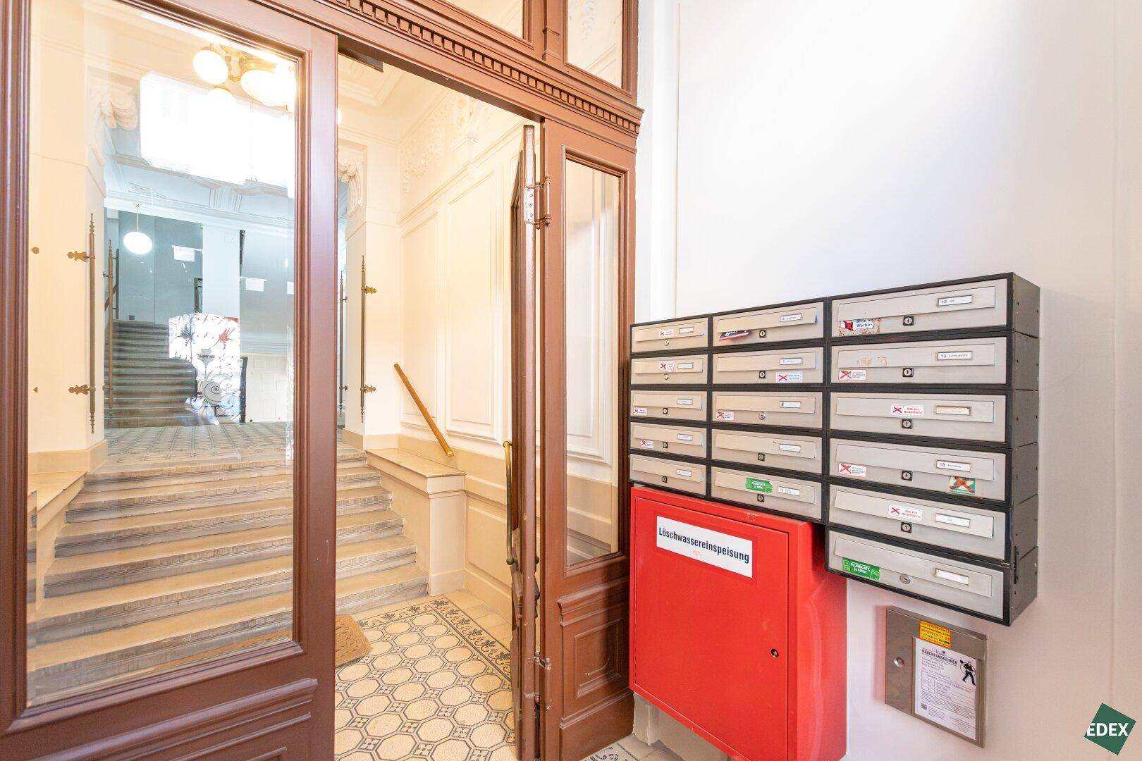 Eingangsbereich eines Altbaus mit Briefkästen und historischer Holztür.