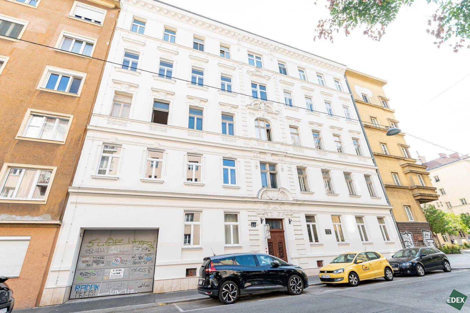 Klassische Altbaufassade mit vielen Fenstern und geparkten Autos auf der Straße.