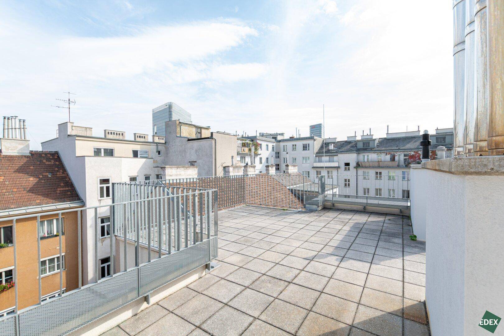 Weitläufige Dachterrasse mit Fliesenboden und Panoramablick über die Dächer der Stadt.