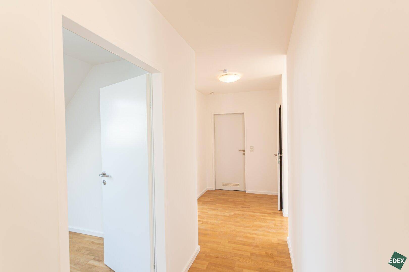 Heller Flur mit Holzparkettboden und weiß gestrichenen Wänden, der zu verschiedenen Räumen führt.