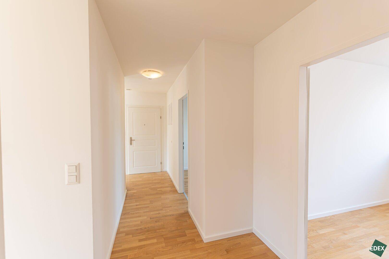 Geräumiger Flur mit Holzparkettboden, weiß gestrichenen Wänden und Spiegelfläche.