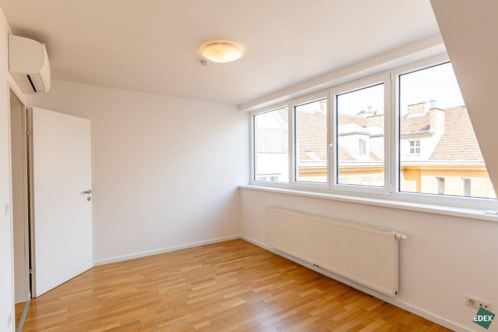 Helles Zimmer mit Holzparkettboden, großen Fenstern und Klimaanlage.