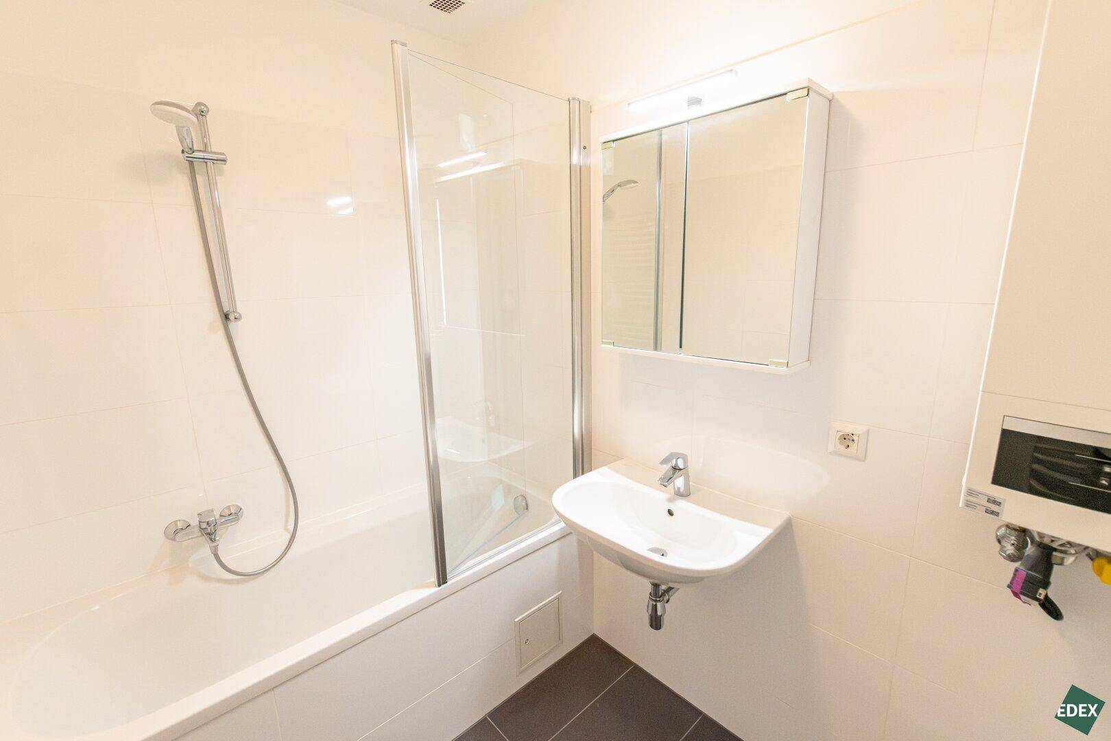 Modernes Badezimmer mit Badewanne, Duschabtrennung, Waschbecken und Wandspiegel.