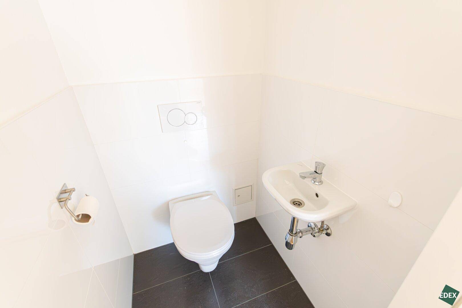 Separates Gäste-WC mit wandhängender Toilette und kleinem Handwaschbecken.