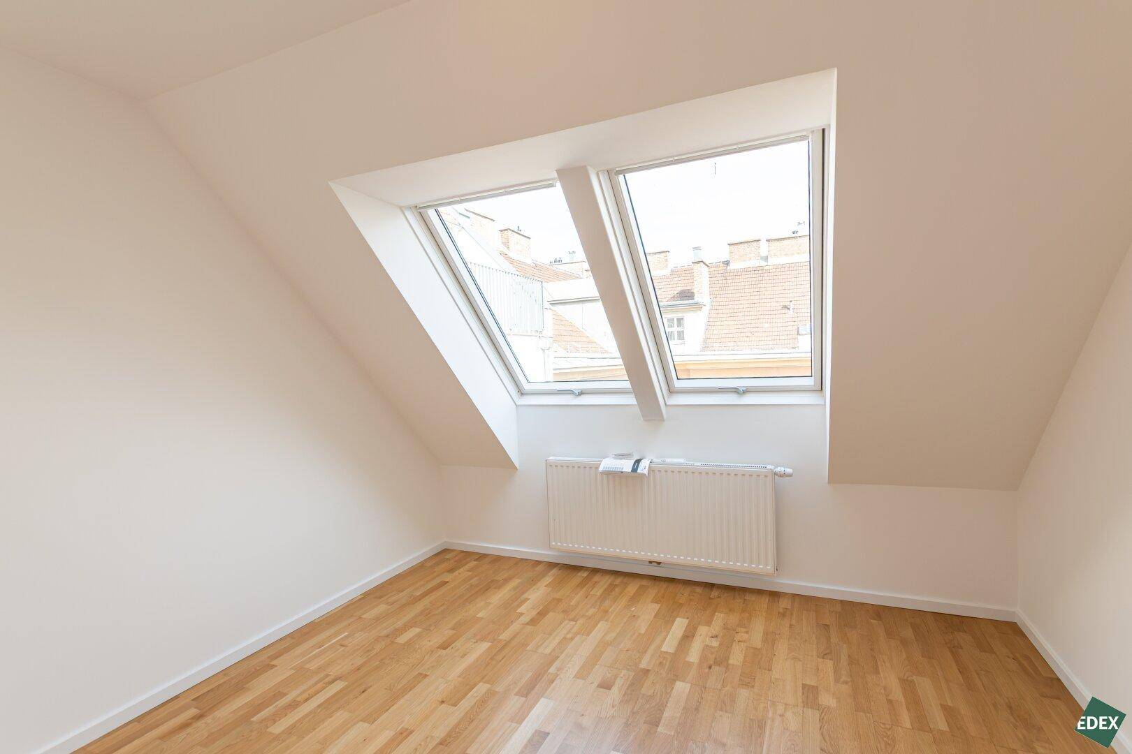 Gemütliches Zimmer mit Dachschräge, Holzparkettboden und zwei Dachfenstern.