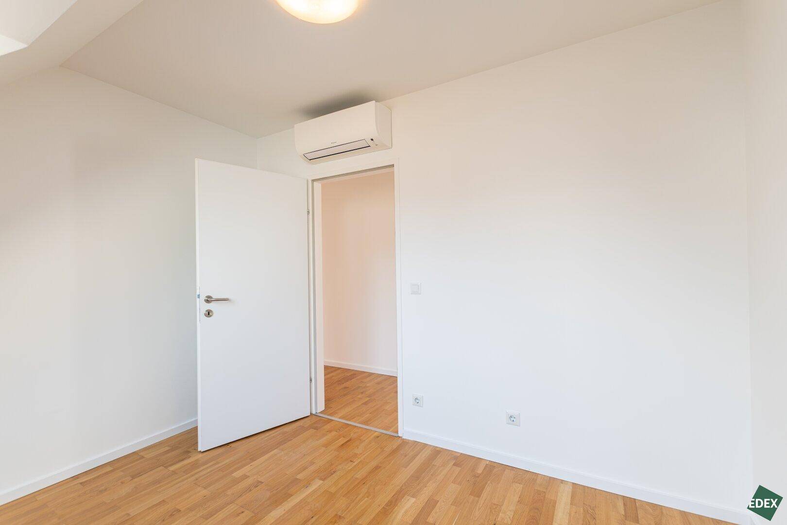 Leeres Zimmer mit Holzparkettboden, weiß gestrichenen Wänden und Klimaanlage.