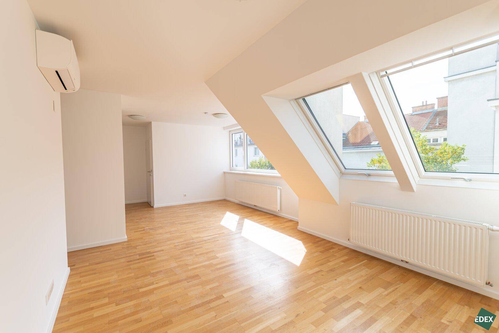 Helles, leeres Zimmer mit Holzparkettboden, Dachschrägen und großen Dachfenstern.