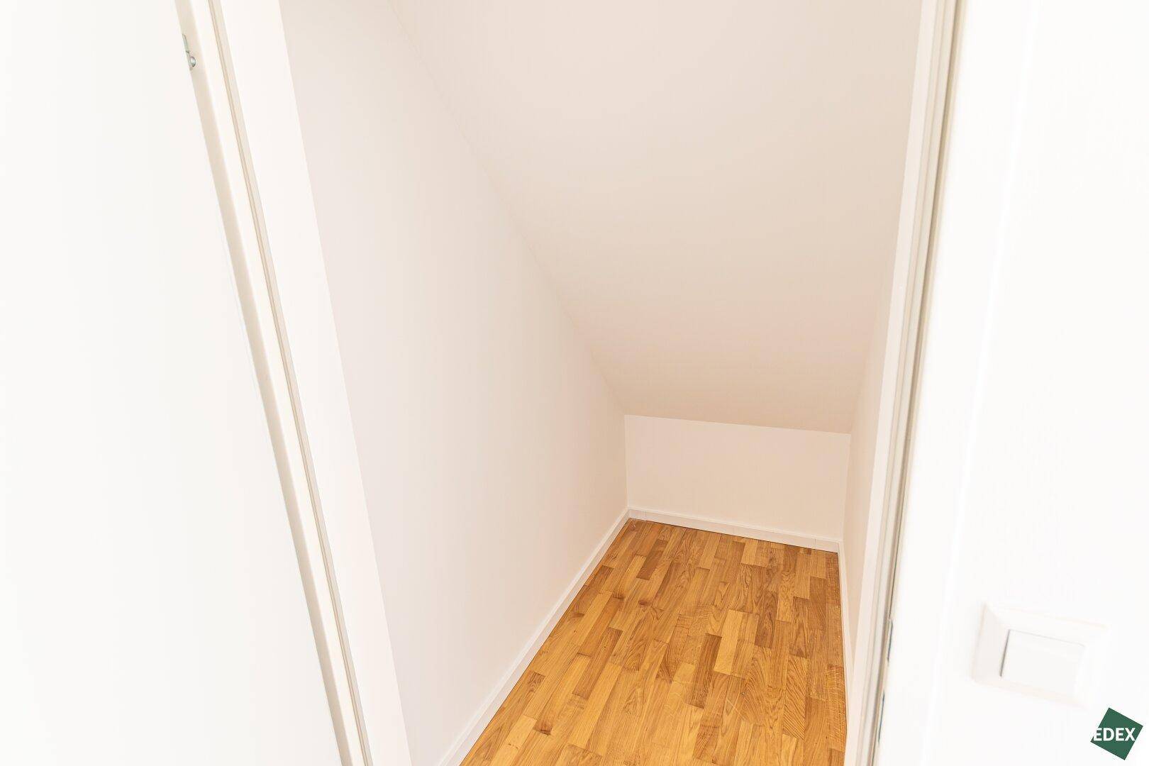 Kleiner Abstellraum unter der Dachschräge mit Holzparkettboden und weißen Wänden.