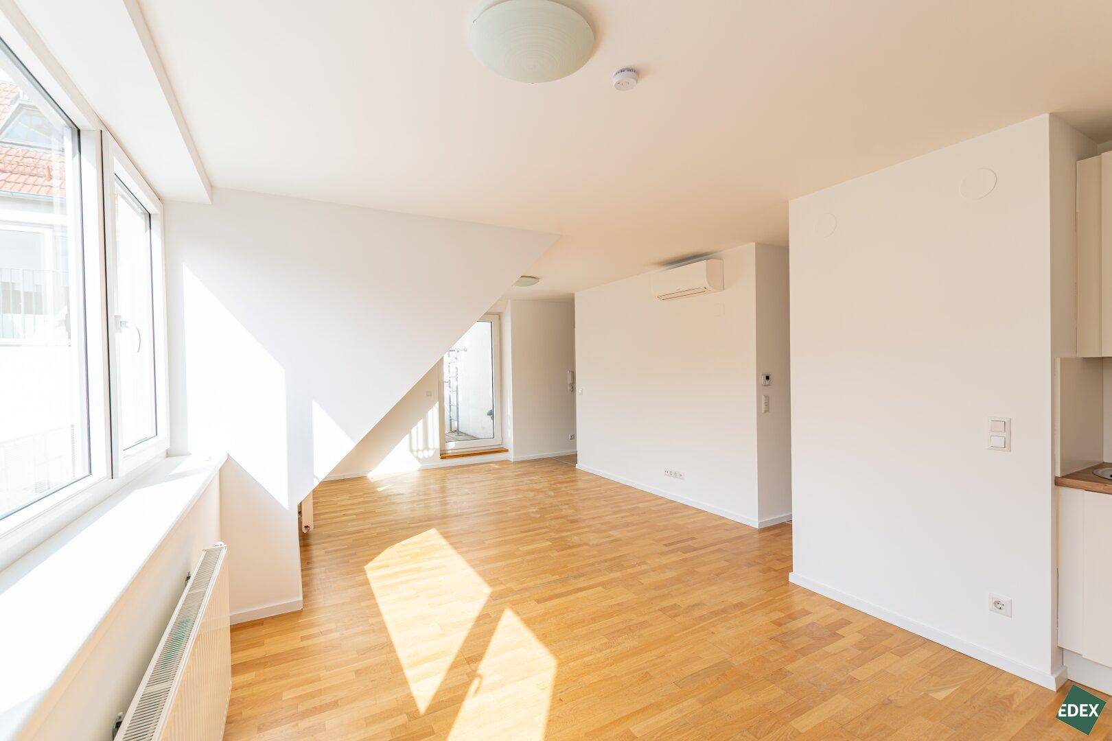 Lichtdurchfluteter Wohnbereich mit Holzparkett, Dachschräge und Zugang zu einem Außenbereich.