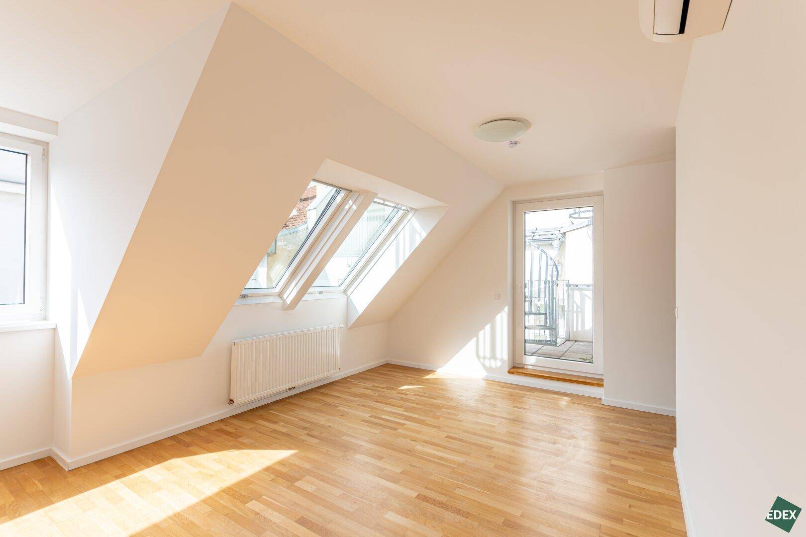 Heller Raum mit Holzparkett, Dachfenstern und Zugang zu einer kleinen Terrasse.