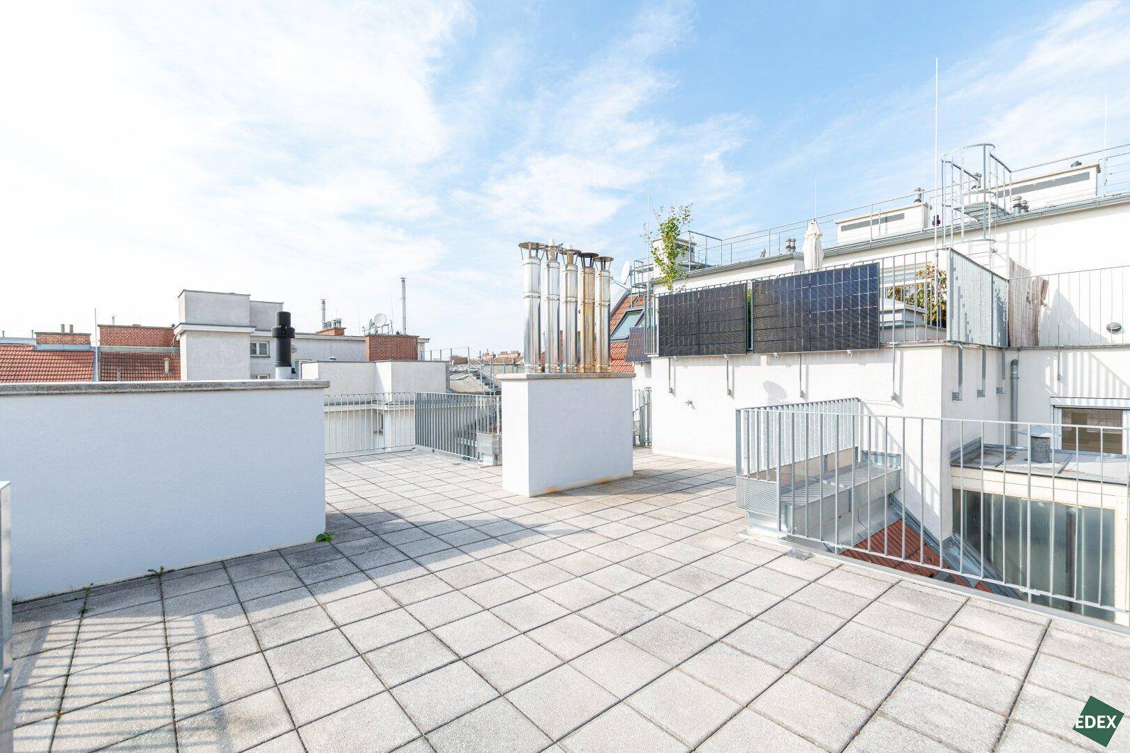 Geräumige Dachterrasse mit Fliesenboden, Metallgeländer und Blick auf die Stadt.