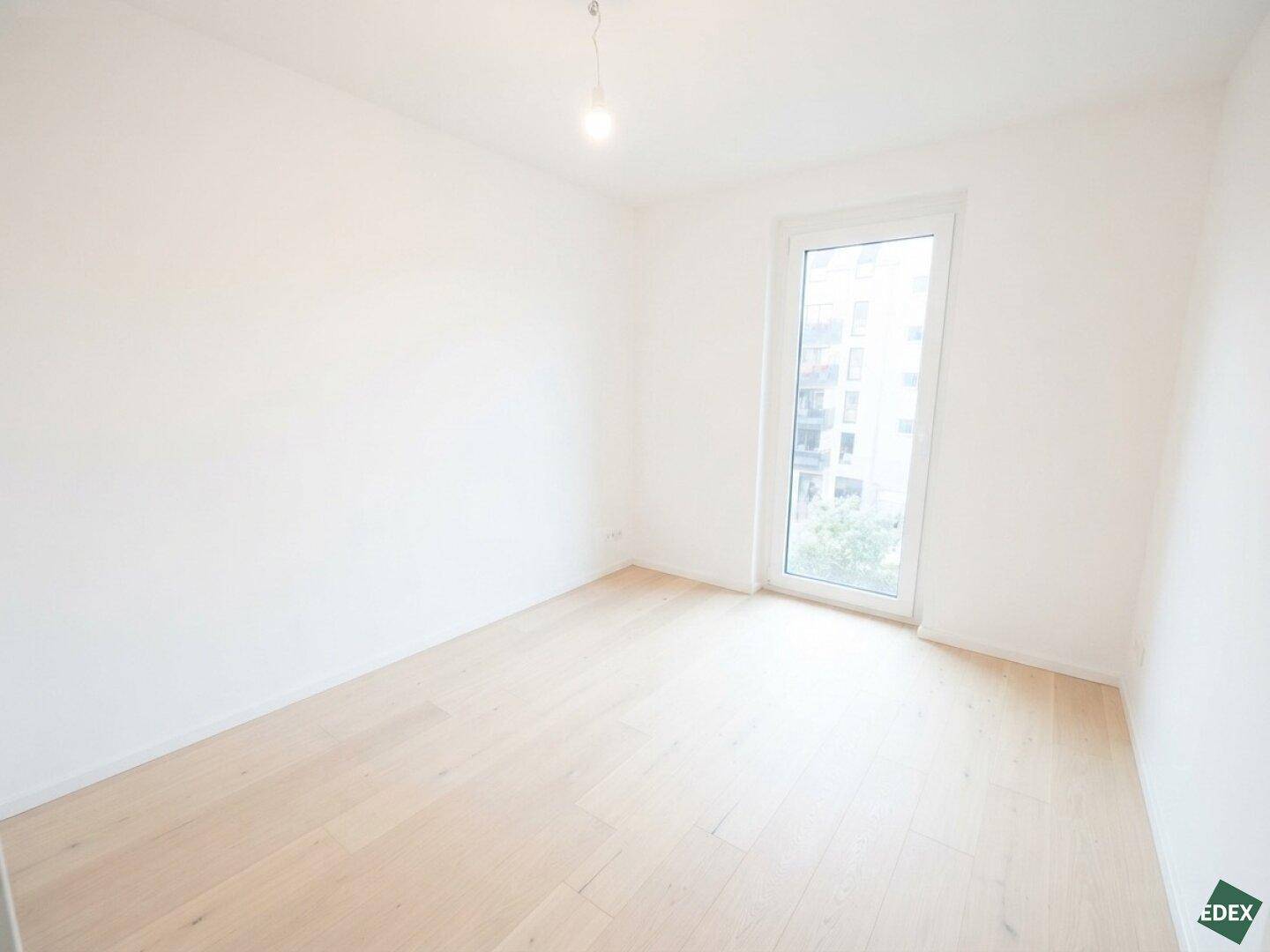 Leeres Schlafzimmer mit hellem Holzboden und großem Fenster für viel Tageslicht.