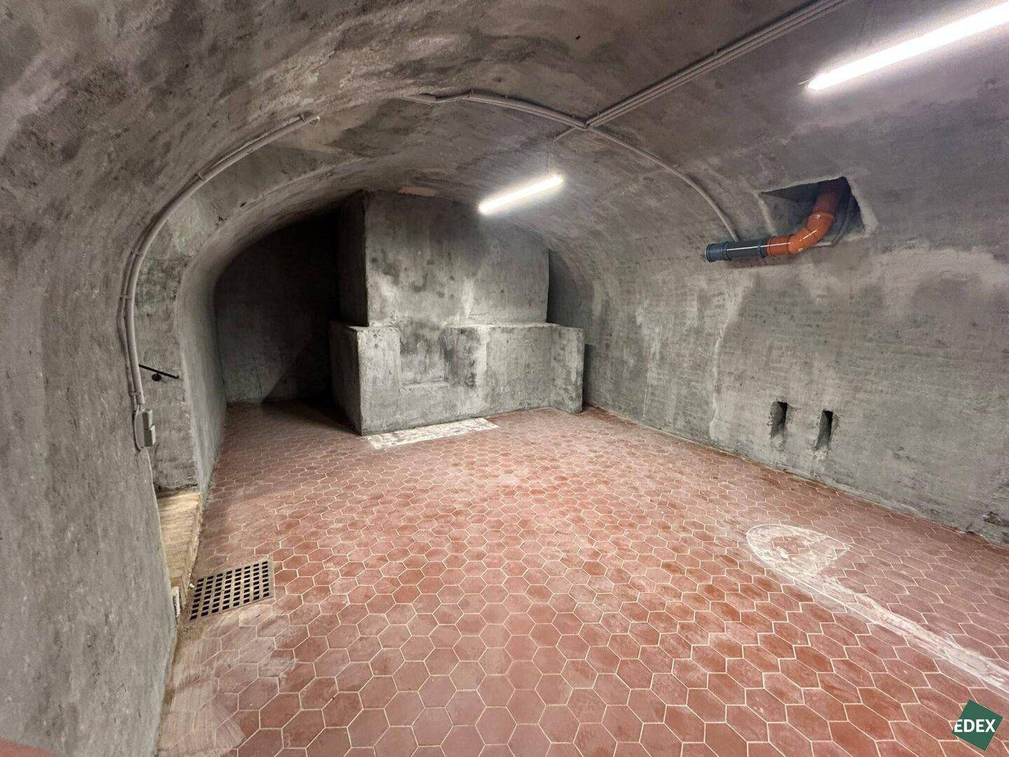 Weiterer Blick in den Kellerraum mit gewölbter Betondecke, Terrakotta-Fliesen und einer gemauerten Struktur.