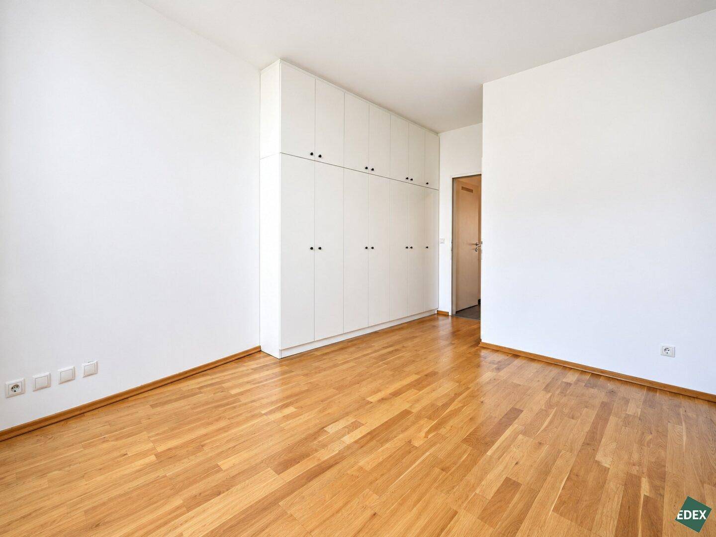 Schlafzimmer mit durchgehendem Einbauschrank und hellem Parkettboden, ideal für Stauraum.